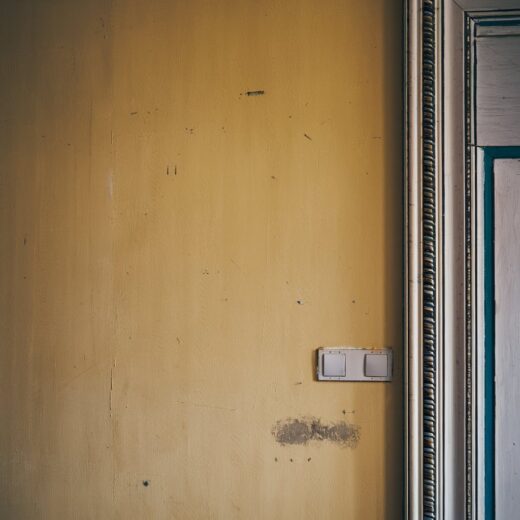 Gelbe Wand einer leerstehenden Wohnung mit Gebrauchsspuren und elektrischen Anschlüssen.