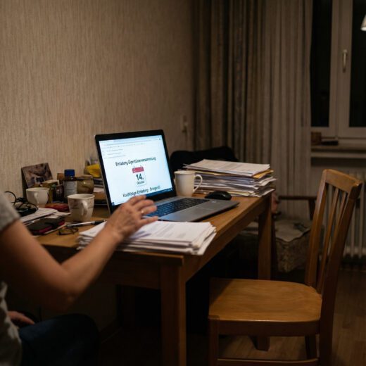 Eine Eigentümerin verschickt vom privaten Schreibtisch eine offizielle Versammlungseinladung mit unzureichender Frist; ein leerer Stuhl steht am Tisch.